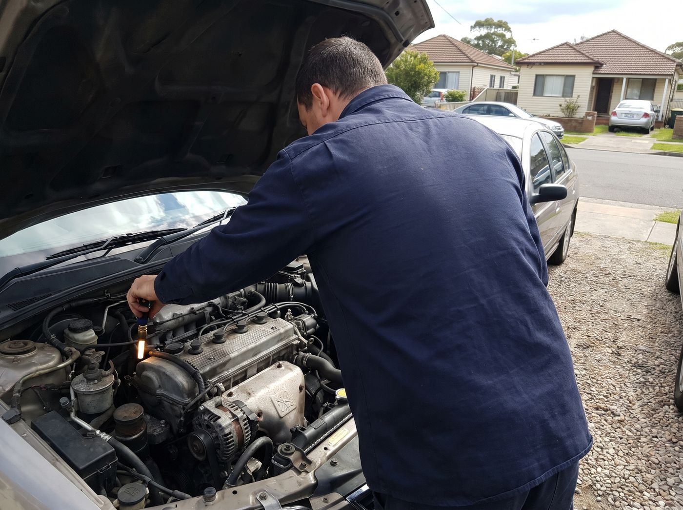 Mechanic checking the engine bay of a used car with a torch (illustrative image)